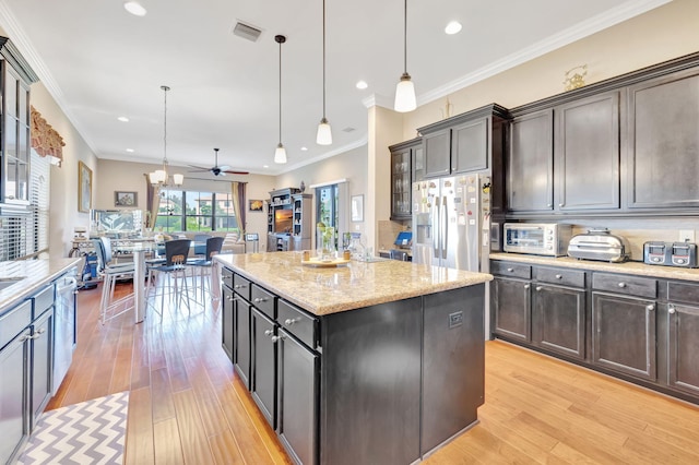 kitchen with appliances with stainless steel finishes, decorative light fixtures, a kitchen island, and light hardwood / wood-style flooring