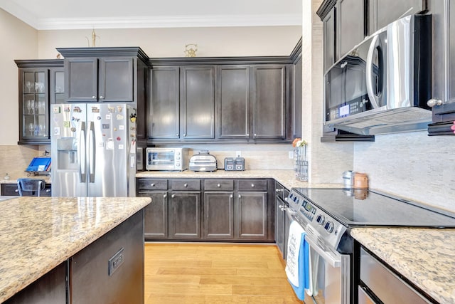 kitchen with light stone countertops, light wood-type flooring, dark brown cabinets, stainless steel appliances, and crown molding