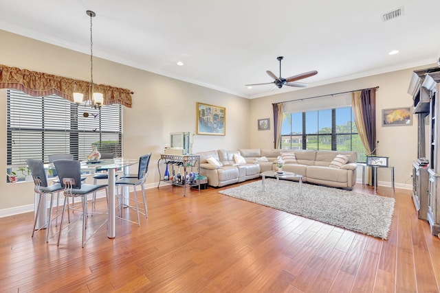 living room featuring ceiling fan with notable chandelier, wood-type flooring, and crown molding