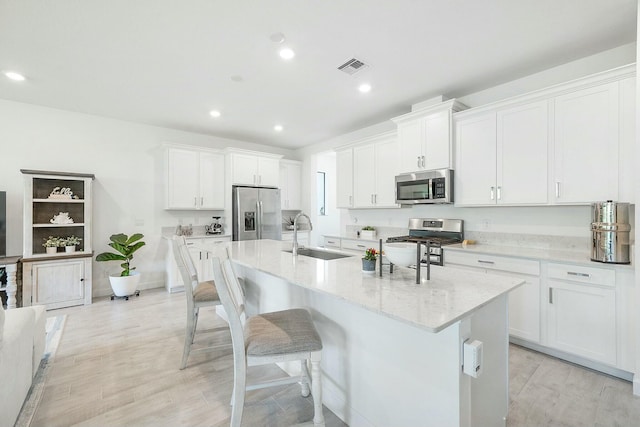 kitchen featuring light stone countertops, sink, stainless steel appliances, light hardwood / wood-style flooring, and white cabinets