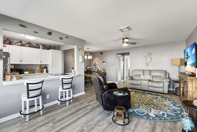 living room with ceiling fan with notable chandelier, light hardwood / wood-style flooring, and sink