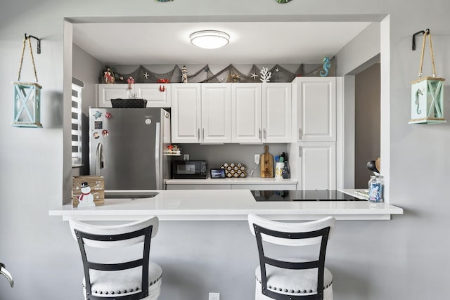 kitchen with black appliances, kitchen peninsula, white cabinetry, and a breakfast bar area