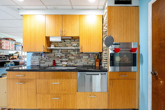 kitchen with appliances with stainless steel finishes, a paneled ceiling, and tasteful backsplash