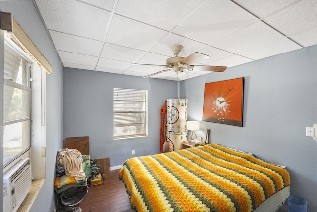 bedroom with hardwood / wood-style floors, ceiling fan, cooling unit, and a drop ceiling