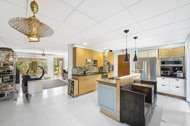 kitchen featuring ceiling fan, a drop ceiling, hanging light fixtures, stainless steel appliances, and tasteful backsplash