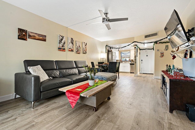 living room with ceiling fan, a textured ceiling, and light wood-type flooring