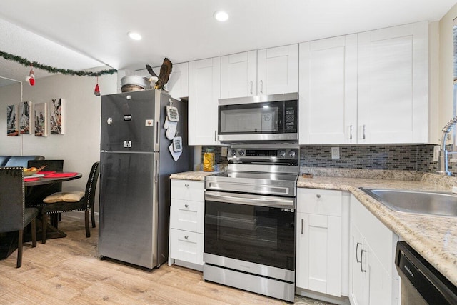 kitchen with white cabinetry, sink, backsplash, light hardwood / wood-style floors, and appliances with stainless steel finishes