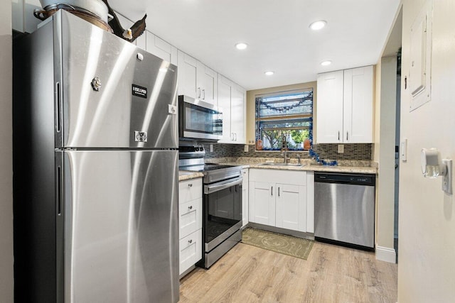 kitchen featuring white cabinetry, sink, light stone counters, light hardwood / wood-style flooring, and appliances with stainless steel finishes