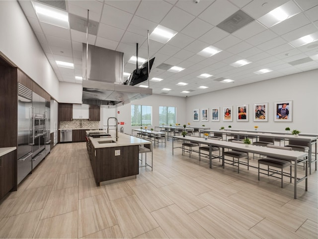 kitchen featuring dark brown cabinetry, a large island, sink, a kitchen bar, and a paneled ceiling