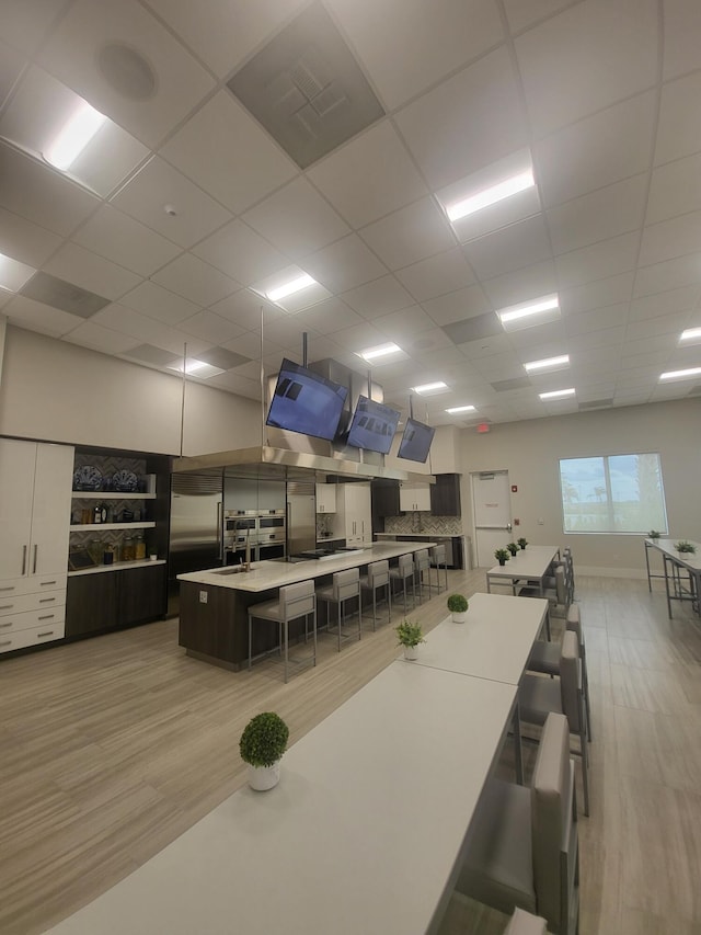 kitchen with a breakfast bar area, a kitchen island with sink, a drop ceiling, and built in refrigerator