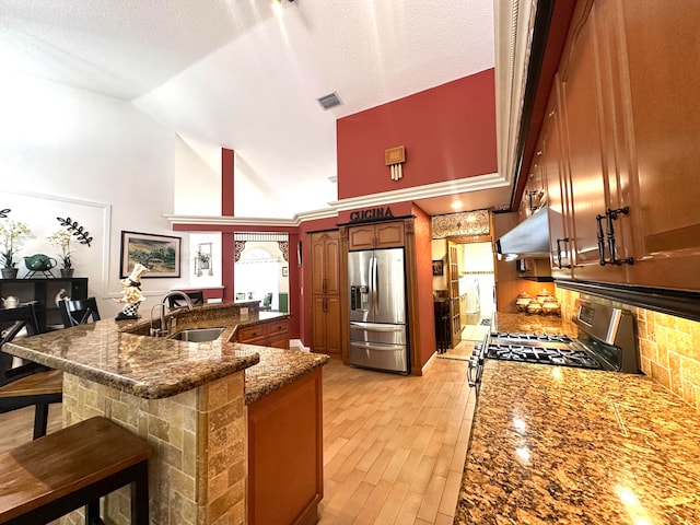 kitchen with a breakfast bar, ventilation hood, sink, a textured ceiling, and appliances with stainless steel finishes