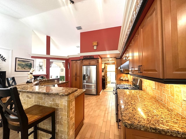 kitchen with a breakfast bar, lofted ceiling, sink, appliances with stainless steel finishes, and kitchen peninsula