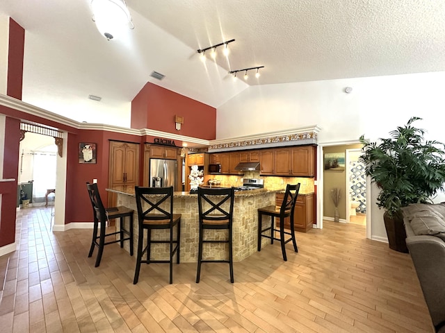 17976 88th Rd N, Loxahatchee, FL 33470 - kitchen with appliances with stainless steel finishes, rail lighting, under cabinet range hood, a kitchen bar, and light wood finished floors