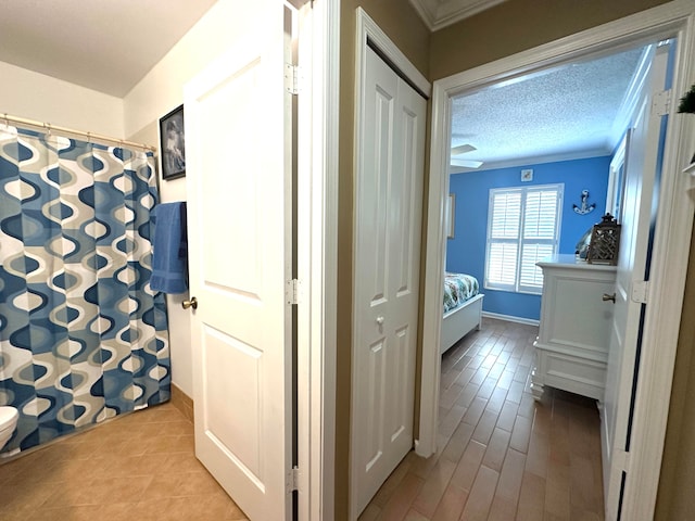 hallway featuring crown molding, a textured ceiling, and light wood-type flooring