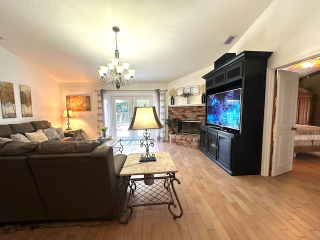 living room featuring a textured ceiling, light wood-type flooring, a fireplace, and a chandelier