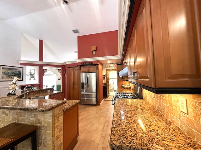 kitchen with dark stone counters, a textured ceiling, sink, high vaulted ceiling, and stainless steel fridge with ice dispenser