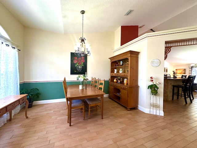 dining space featuring a textured ceiling, lofted ceiling, a notable chandelier, and light wood-type flooring