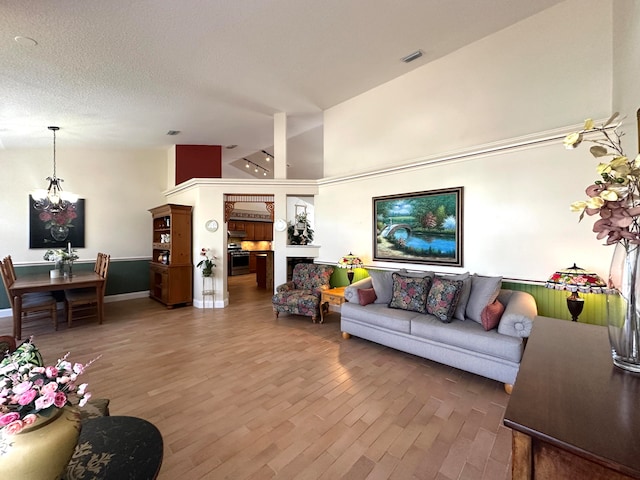 living room featuring a textured ceiling, high vaulted ceiling, a notable chandelier, and hardwood / wood-style flooring