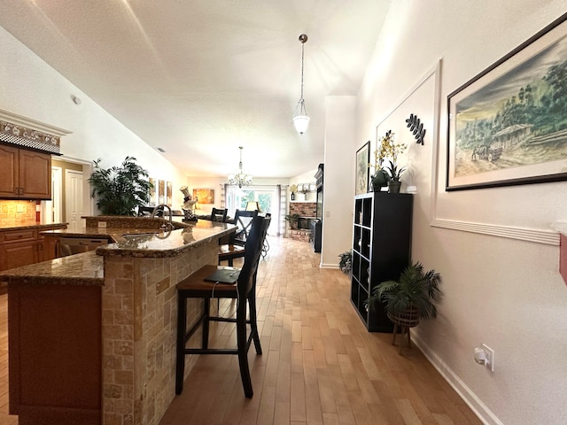 kitchen with pendant lighting, vaulted ceiling, dark stone countertops, light wood-type flooring, and a breakfast bar area