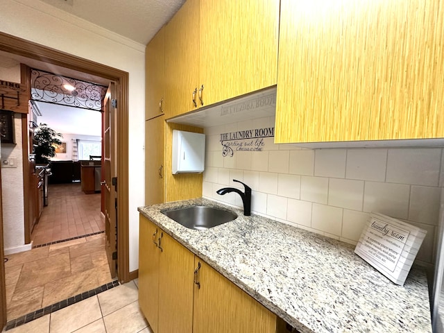 kitchen with decorative backsplash, light stone counters, sink, and a textured ceiling