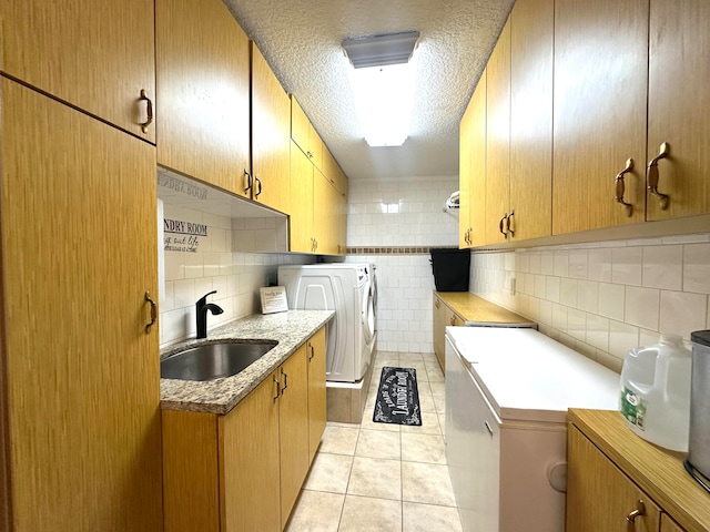 kitchen with sink, independent washer and dryer, a textured ceiling, light tile patterned floors, and tile walls