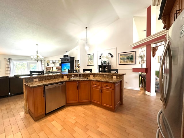 kitchen with sink, hanging light fixtures, stainless steel appliances, dark stone countertops, and vaulted ceiling