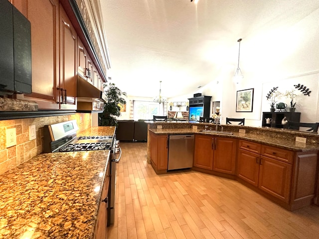 kitchen featuring hanging light fixtures, dark stone countertops, lofted ceiling, appliances with stainless steel finishes, and light wood-type flooring