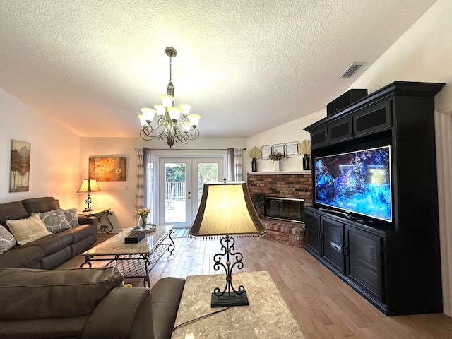 living room featuring french doors, a brick fireplace, a textured ceiling, light hardwood / wood-style floors, and a chandelier