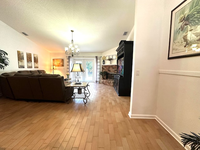 living room with an inviting chandelier, wood-type flooring, a textured ceiling, and a brick fireplace