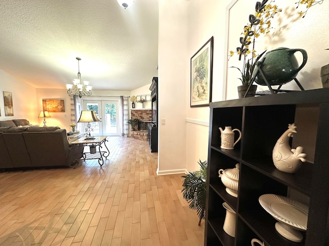 corridor with light hardwood / wood-style floors, french doors, a textured ceiling, and a chandelier