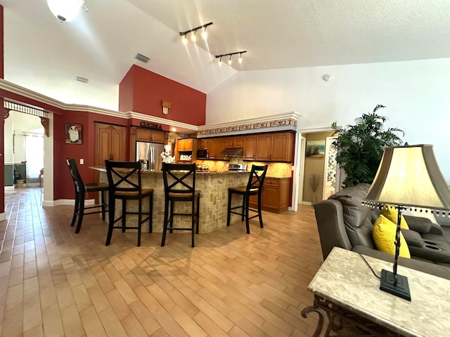 kitchen featuring a breakfast bar, high vaulted ceiling, track lighting, stainless steel fridge, and light hardwood / wood-style floors