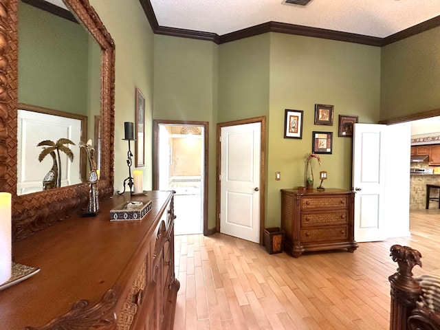 hall with crown molding, a towering ceiling, a textured ceiling, and light wood-type flooring