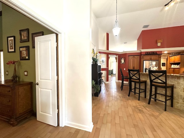 hallway with high vaulted ceiling and light hardwood / wood-style flooring