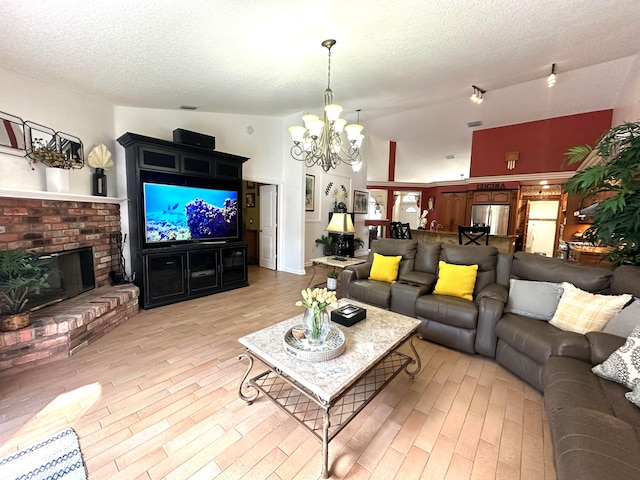 living room with a brick fireplace, a textured ceiling, light hardwood / wood-style floors, and an inviting chandelier