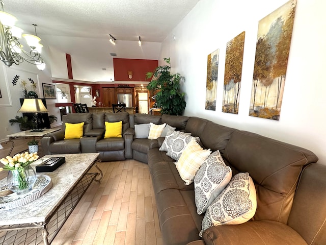 living room featuring a textured ceiling, hardwood / wood-style floors, a chandelier, and lofted ceiling