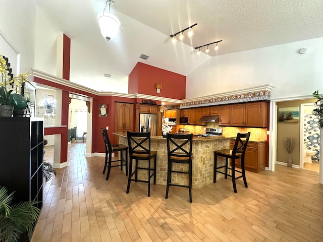 kitchen with light hardwood / wood-style flooring, high vaulted ceiling, a breakfast bar area, decorative backsplash, and appliances with stainless steel finishes