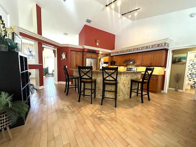 kitchen with high vaulted ceiling, track lighting, a kitchen breakfast bar, light hardwood / wood-style flooring, and stainless steel appliances