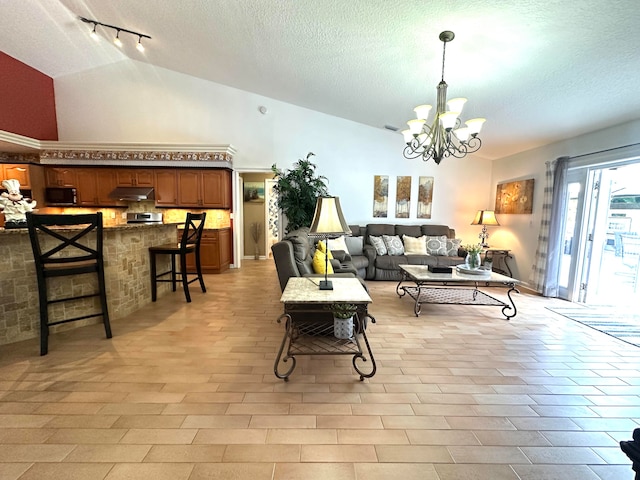 living room with a chandelier, a textured ceiling, rail lighting, and high vaulted ceiling