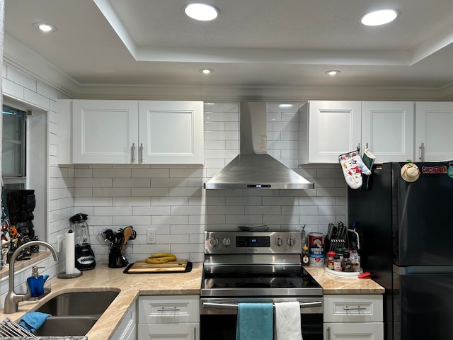 kitchen with sink, wall chimney range hood, black fridge, stainless steel range with electric cooktop, and white cabinets