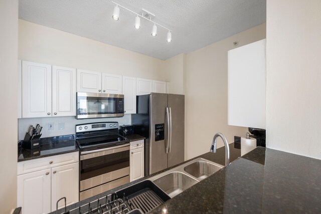 kitchen featuring dark stone countertops, white cabinetry, a textured ceiling, and appliances with stainless steel finishes