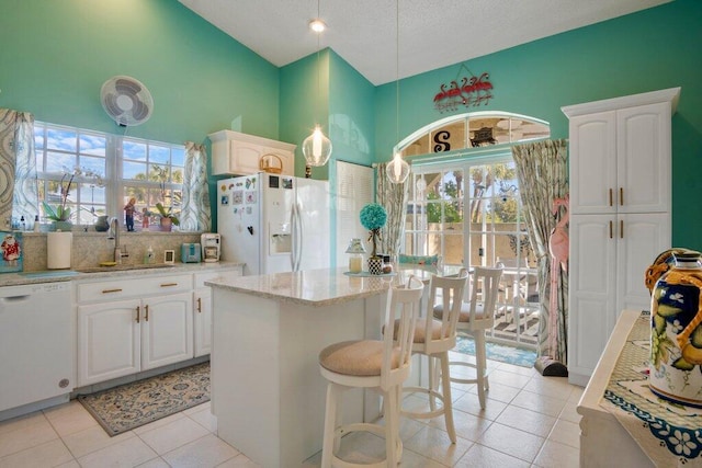 kitchen with a center island, sink, light tile patterned floors, white appliances, and white cabinets