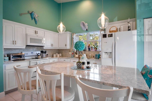 kitchen with white appliances, light tile patterned floors, light stone countertops, a towering ceiling, and white cabinetry