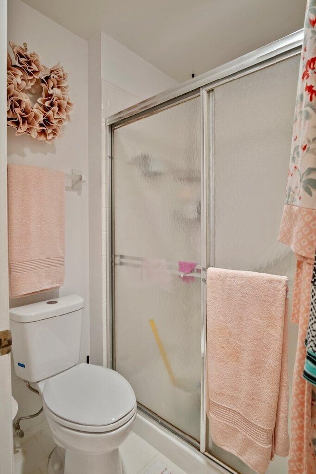 bathroom featuring tile patterned floors, a shower with door, and toilet