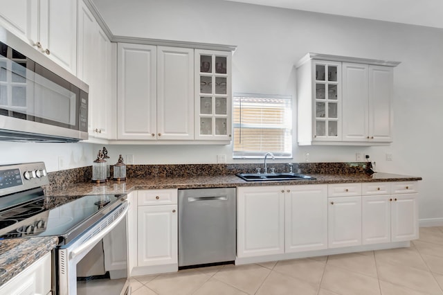 kitchen with sink, stainless steel appliances, white cabinets, dark stone counters, and light tile patterned flooring