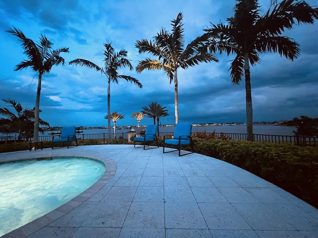 pool at dusk featuring a patio area and a water view