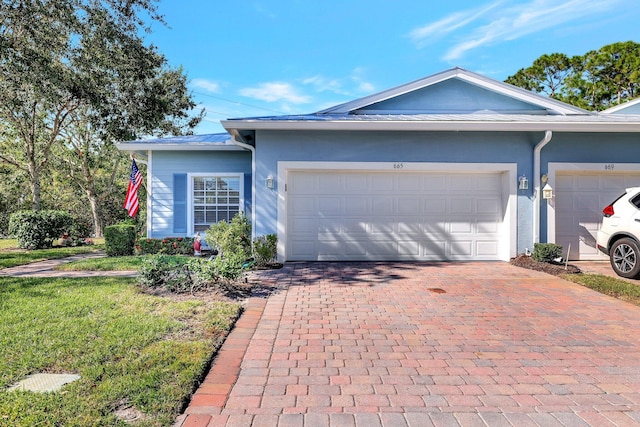 single story home featuring a front lawn, decorative driveway, an attached garage, and stucco siding