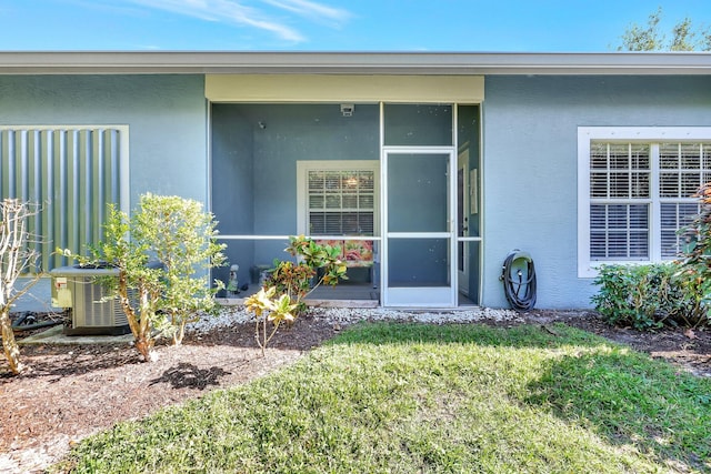 view of exterior entry with a lawn, cooling unit, and stucco siding