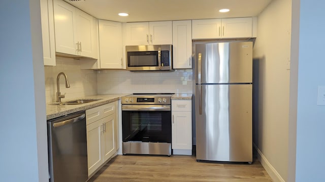 kitchen with white cabinets, sink, light wood-type flooring, appliances with stainless steel finishes, and light stone counters