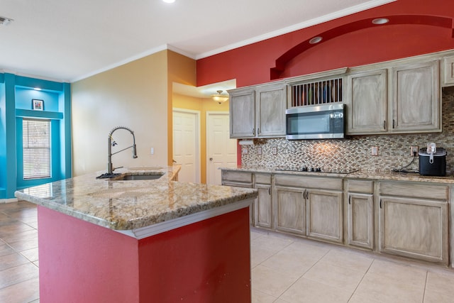 kitchen with sink, light stone counters, an island with sink, black electric stovetop, and ornamental molding