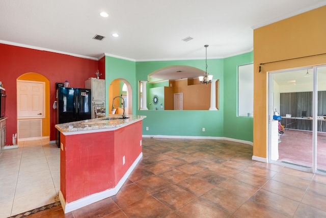 kitchen featuring sink, hanging light fixtures, an inviting chandelier, black refrigerator, and a center island with sink